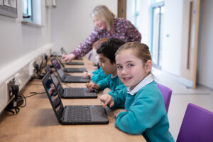 Children on laptops, teacher supporting.